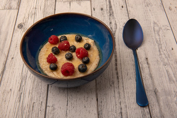 Bowl of porridge with raspberries, blueberries and honey on a wooden background 