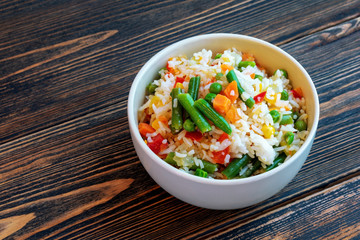 A Cup of white rice with vegetables on a dark wooden background. Prepared without loss of vitamins.