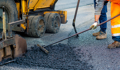 Worker regulate tracked paver laying asphalt heated to temperatures above 160 ° pavement on a runway