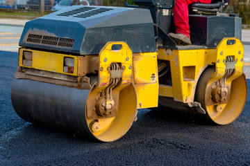 Worker leads the vibrating road roller to compact the asphalt laid out for the construction of a road