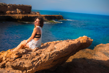 Fototapeta na wymiar Model sitting on edge of rocks with sea view 