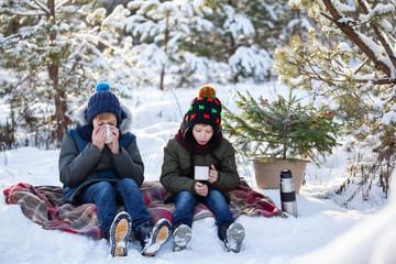 Adorable two brothers sitting on plaid and drinking chocolate or hot tea in sunny winter day.