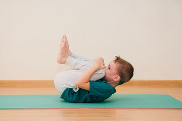 Fototapeta na wymiar Cute little boy is learning to do yoga in the gym