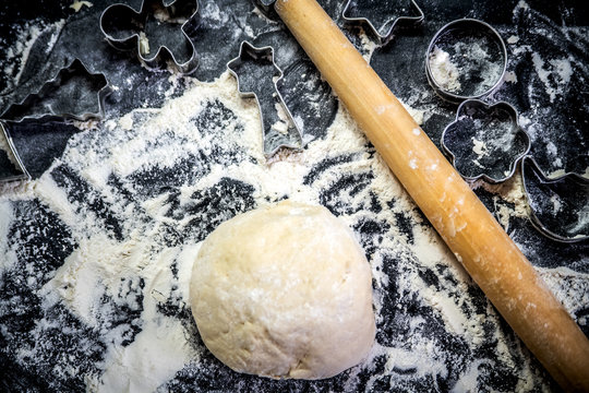 Kneaded dough, rolling pin and cookie cutters on a table covered with flour.