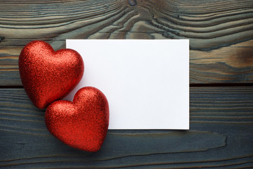 Blank paper message with two red love hearts on wooden background