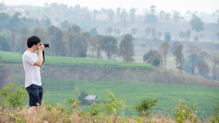 Asian man traveler using digital camera taking photo of mountain view landscape. Travel lifestyle or nature photography concepts