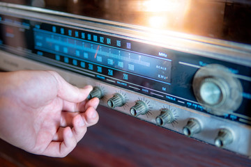 Male hand turning retro radio button. Listen to music or news with old classic radio receiver. Vintage lifestyle