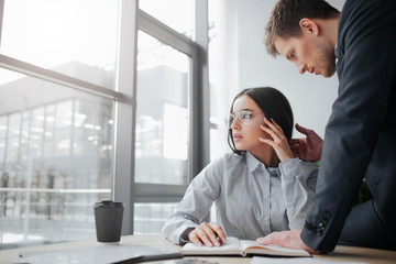 Afraid and scare young woman sit at table and look at window. Guy touch her face and hair. He wants to discriminate her.