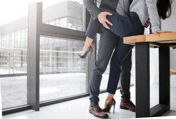 Cut view of man in suit stand and hold woman's leg in sexual pose. She sit on table. They are in...
