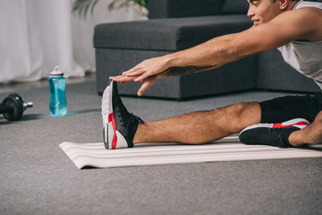 cropped view of mixed race man stretching on fitness mat in living room