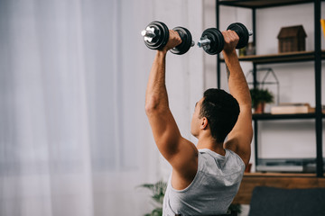muscular amixed race man holding heavy dumbbells over head