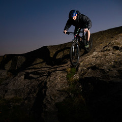 Naklejka na ściany i meble Cyclist Riding the Bike on Rocky Trail at Night. Extreme Sport and Enduro Biking Concept.