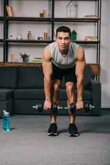 handsome mixed race man workout with dumbbells near sport bottle