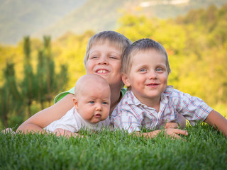 Naklejka na ściany i meble Three brothers are lying on a green meadow. Emotions of children. Vacation with children. Childcare. Goods for kids. Sun protection. Child development.