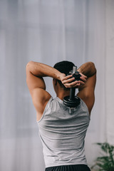 back view of man standing in sportswear and holding dumbbell