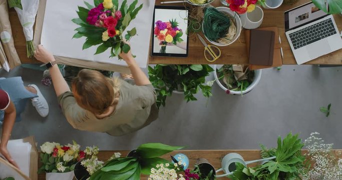 multi ethnic business woman florist in vibrant flower shop wrapping beautiful bouquet preparing successful sales order working together above view