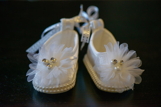 Adorable white baby girl shoes with pearl details and sparkly decorations. Horizontal shot of baby girl elegant white shoes with pearl details and tulle for festivities and formal events.