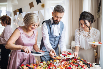 Multigeneration family putting food on plates on a indoor family birthday party.