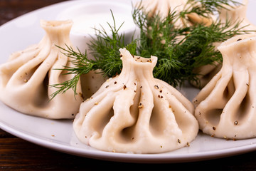 Boiled khinkalis with meat and pepper, is served with sour cream and fennel