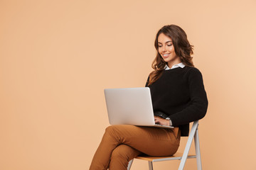 Beautiful amazing young woman posing isolated sitting on stool using laptop computer.