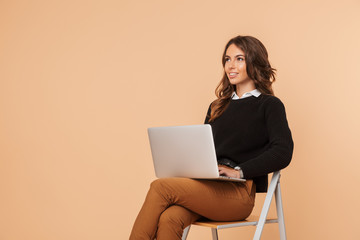 Beautiful amazing young woman posing isolated sitting on stool using laptop computer.