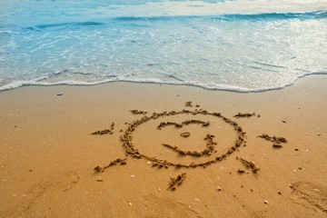 Writing sun smile on sand beach with blue waves ocean.