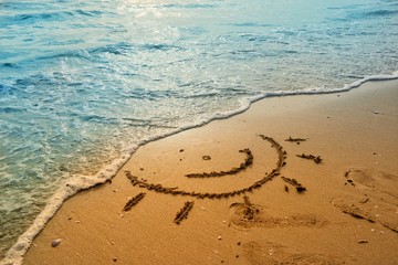 Writing sun smile on sand beach with blue waves ocean.