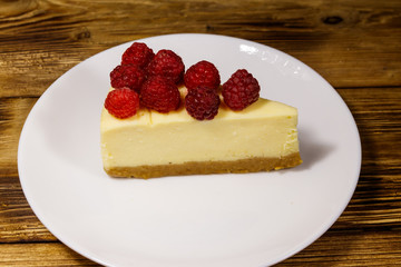Piece of tasty New York cheesecake with raspberries in a white plate on wooden table