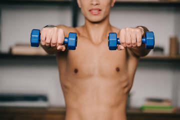 Fototapeta na wymiar cropped view of mixed race man exercising with blue dumbbells