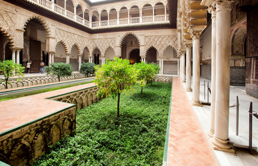 Fototapeta premium Green courtyard of Alcazar, example of Mudejar architecture of the 14th century, historical royal palace with trees