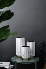 Isolated composition of white marble ceramic vase on green metal side table in artificial plants and stack books scene on gray painted wall background / object isolation / interior design scene