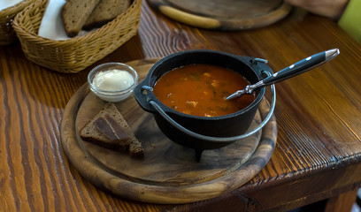 Russian soup, borsch, in a cast iron pot on the background of rye bread, on a wooden table in a stylish restaurant, in the old Russian style