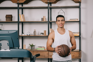 smiling mixed race man holding basketball in living room