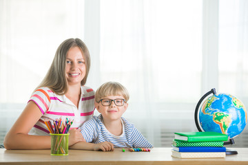 Adorable child studying with his mother at home. Family doing homework together. Young mom helping her son to learn a task.