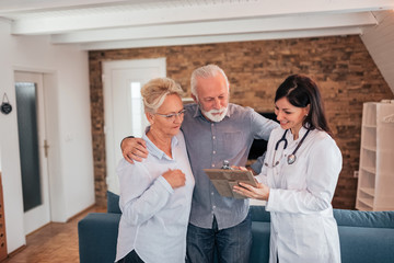 Senior couple discussing with female doctor with while standing in the living room.