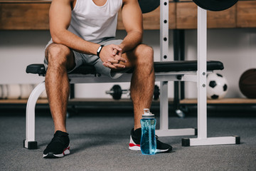 Fototapeta na wymiar cropped view of man sitting with fitness watch near sport bottle