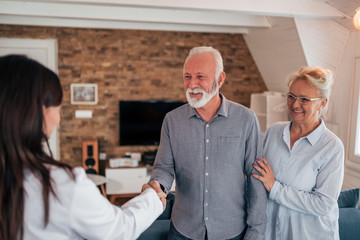 Senior couple welcoming female doctor during home visit.