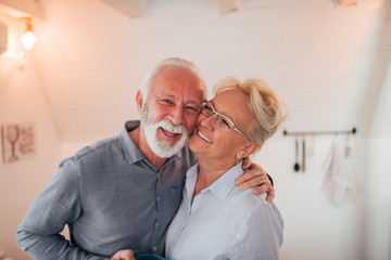 Portrait of a charming senior couple indoors. Smiling and hugging.