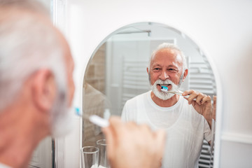 Senior man brushing teeth in the bathroom.