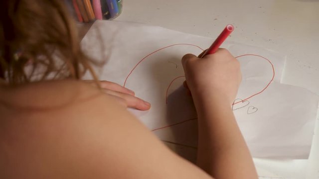 A little girl draws a red heart on a paper
