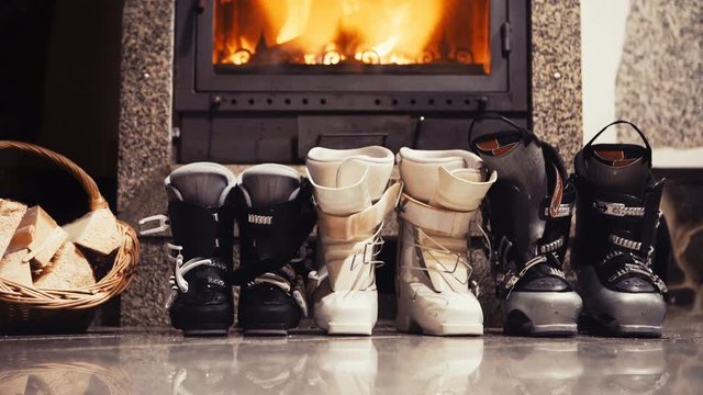 4K Static footage of three pairs of skiing boots standing next to the fireplace. Winter holidays concept.