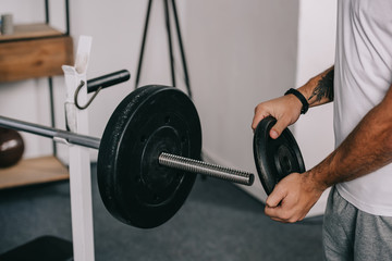 cropped view of man putting disk on barbell