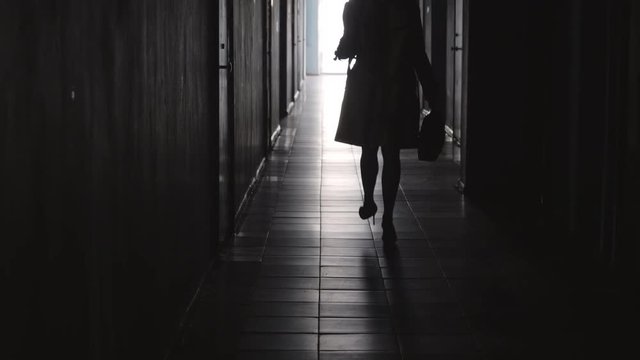 Rear view of silhouette of businesswoman wearing coat and high heels walking away from the camera along hallway in office center