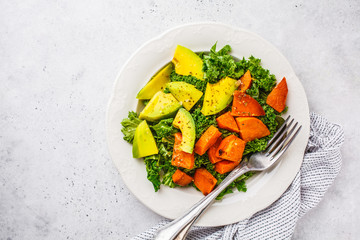 Healthy green kale salad with avocado and baked sweet potatoes, copy space. Plant based diet concept, detox food.