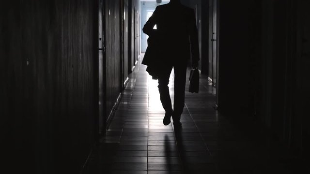 Rear view of silhouette of unrecognizable businessman with briefcase walking away from the camera along hallway in office center