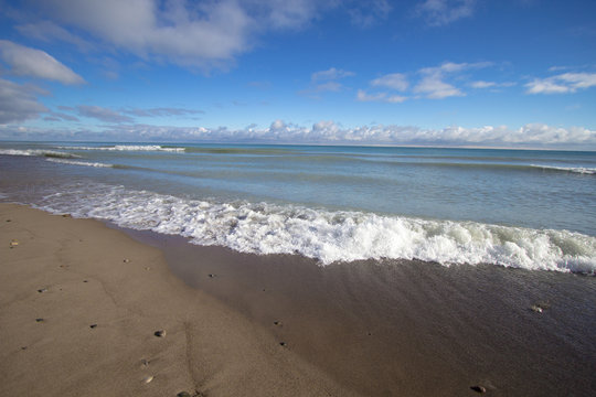 Surf Beach Background. Waves rolls into a wide sandy beach on a sunny summer day. Horizontal orientation with copy space in foreground.