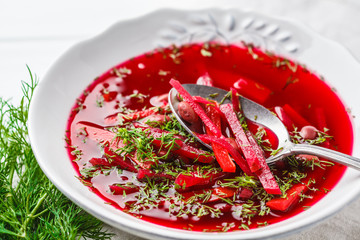 Vegetarian beet soup with beans and vegetables in white plate on white wooden background.