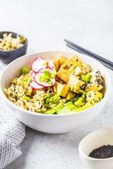 Vegan poke bowl with pickled tofu, vegetables and rice in a white bowl.