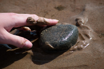 Female hand touches pebble on beach