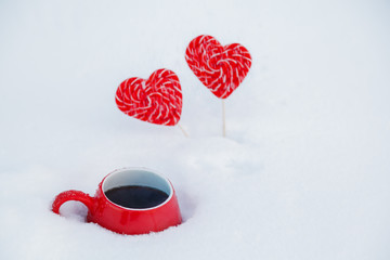 Red mug with hot tea or coffee and lollipops hearts in the snow. The concept of celebrating Valentine's day